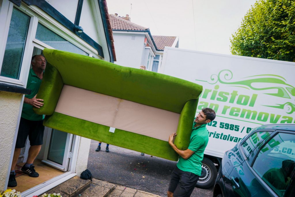 Two members of the BVR team carrying a large green sofa out of a home and into their van.