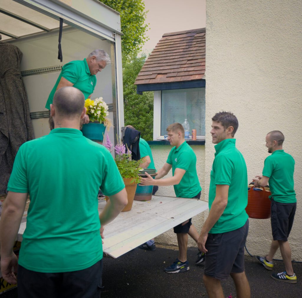 Several movers from Bristol Van Removals, working together to put outdoor potted plants and other items in a van.