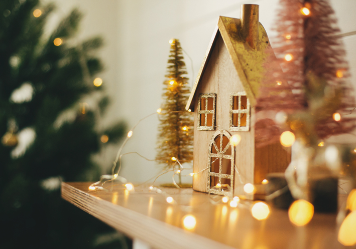 A wooden model of a house surrounded by fairy lights and Christmas ornaments