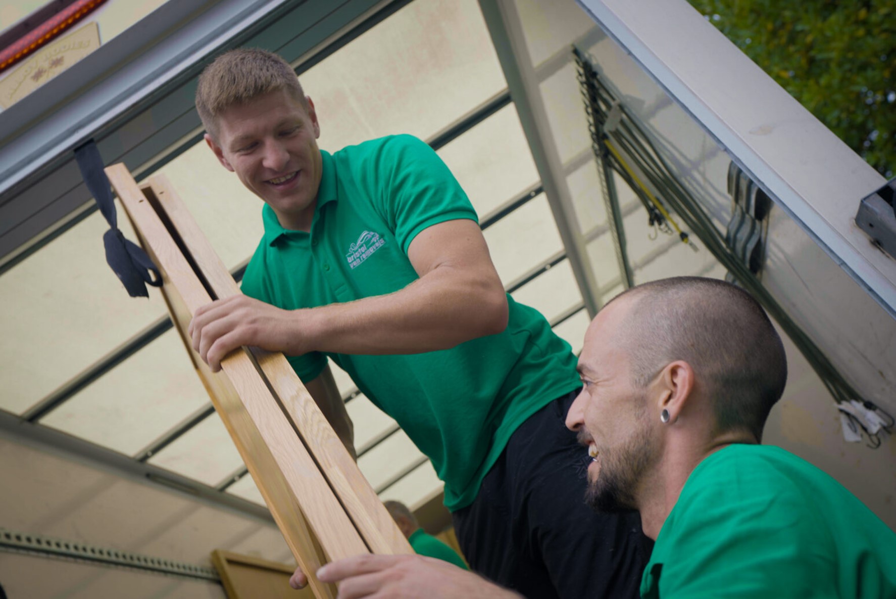 Two movers at Bristol Van Removals handling a piece of furniture, smiling