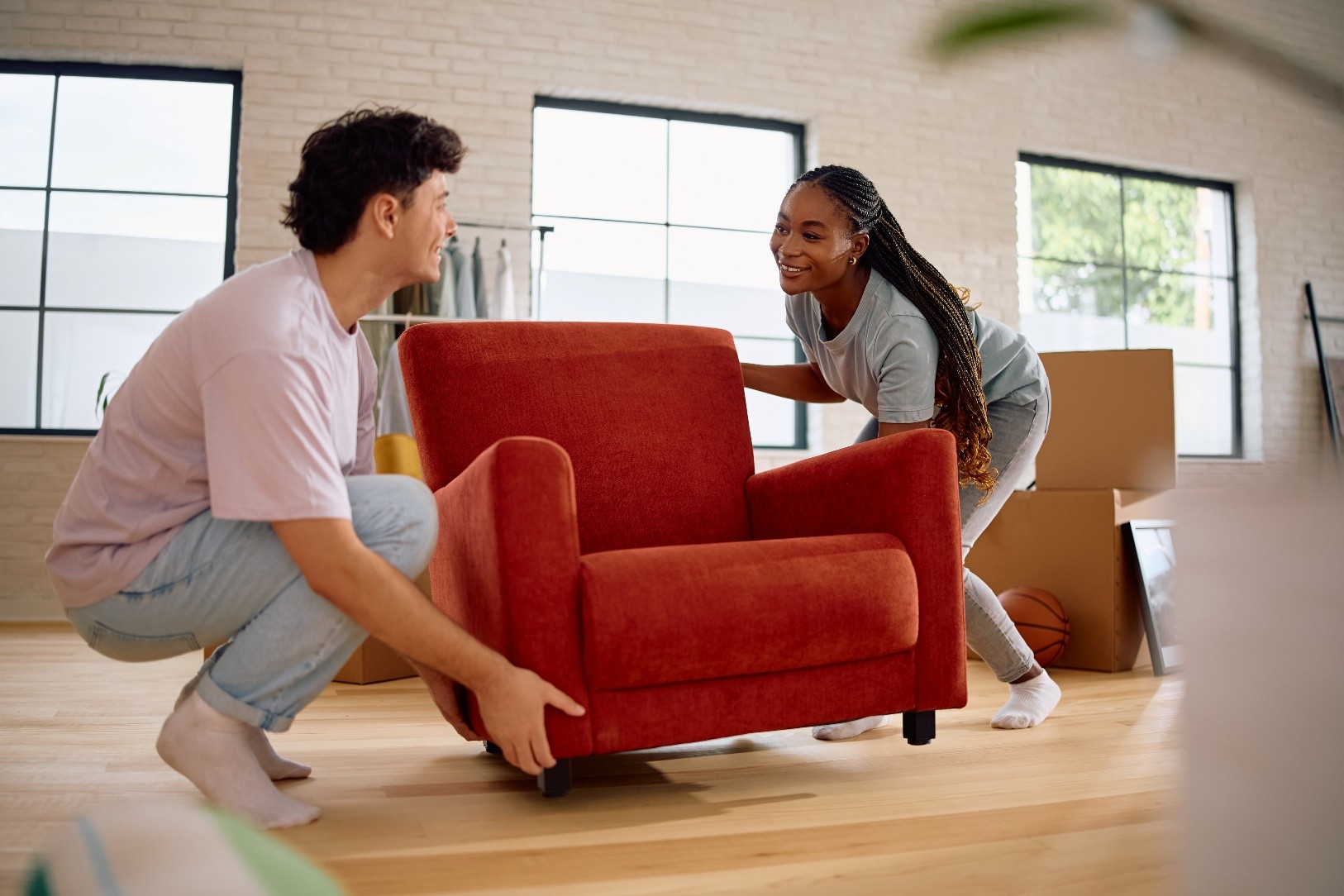 Two young people moving home, lifting a small red couch.